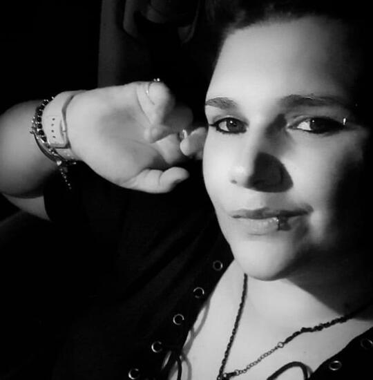 Ritratto in bianco e nero di Manaltea, leggermente di profilo, con lo sguardo sereno e un accenno di sorriso, dita appoggiate delicatamente sulla guancia.